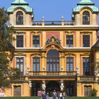 Barockes Schloss mit gelber Fassade und grünen Dächern, umgeben von Bäumen. Menschen stehen vor dem Eingang., © Tourismus & Events Ludwigsburg