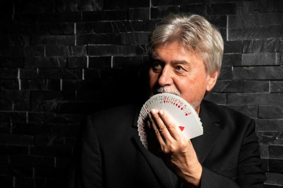 Mann mit grauen Haaren hält Spielkartenfächer vor Gesicht, dunkle Steinwand im Hintergrund., © Horst Reutter