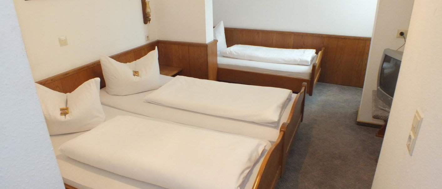 Ein Dreibettzimmer mit zwei Einzelbetten nebeneinander und einem Einzelbett im Hintergrund. Ein Fernseher steht in der Ecke, ein Bild hängt an der Wand., © Gasthof zum Bären
