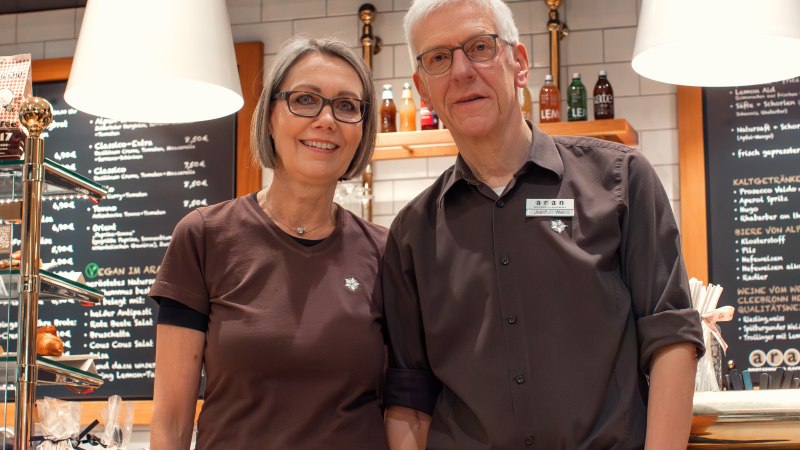 Zwei Personen stehen l&auml;chelnd vor einem Caf&eacute; namens 'aran', das Brotgenuss und Kaffeekultur anbietet., &copy; Cafe aran