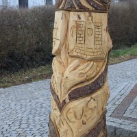 Holzskulptur mit geschnitzten Motiven, darunter ein Gesicht und Gebäude, auf einem gepflasterten Weg am Skulpturenpfad Böbingen., © Gemeinde Böbingen