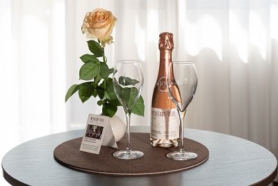 Flasche Rosé Sekt, zwei Gläser und eine Rose auf einem runden Tisch vor einem weißen Vorhang., © Hotel Weinstadt