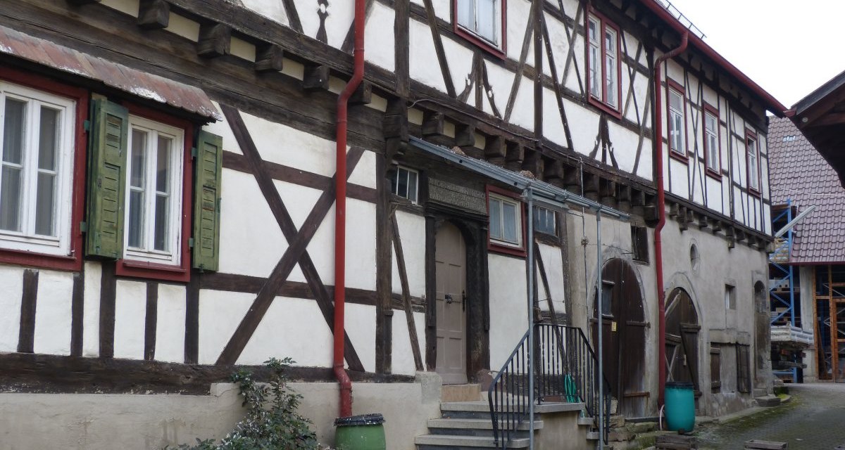 Historisches Fachwerkhaus mit Holzbalken, roten Fensterl&auml;den und gr&uuml;nen Regentonnen. Treppe f&uuml;hrt zur Eingangst&uuml;r. Hof mit Pflastersteinen., &copy; Land der 1000 H&uuml;gel - Kraichgau-Stromberg