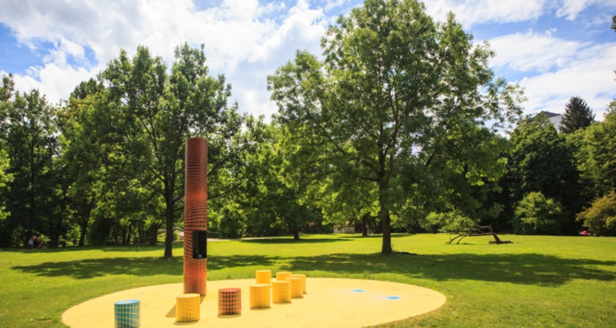 Kunstinstallation im Freien mit bunten Säulen auf gelbem Boden, umgeben von grünen Bäumen und blauem Himmel., © Kai Köpf Kunstinstallation im Freien mit bunten Säulen auf gelbem Boden, umgeben von grünen Bäumen und blauem Himmel., © Kai Köpf