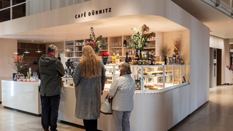 Theke mit Getränken und Kuchenvitrine, dekoriert mit Pflanzen. Drei Personen stehen an., © SMG, Sarah Schmid Theke mit Getränken und Kuchenvitrine, dekoriert mit Pflanzen. Drei Personen stehen an., © SMG, Sarah Schmid
