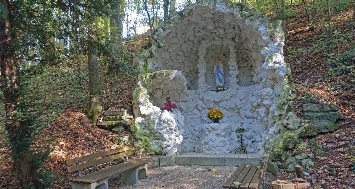 Die Lourdesgrotte in Böbingen zeigt eine Marienstatue in einer steinernen Nische, umgeben von Wald. Vor der Grotte stehen Holzbänke., © Foto: Cornelia Steinbach Die Lourdesgrotte in Böbingen zeigt eine Marienstatue in einer steinernen Nische, umgeben von Wald. Vor der Grotte stehen Holzbänke., © Foto: Cornelia Steinbach