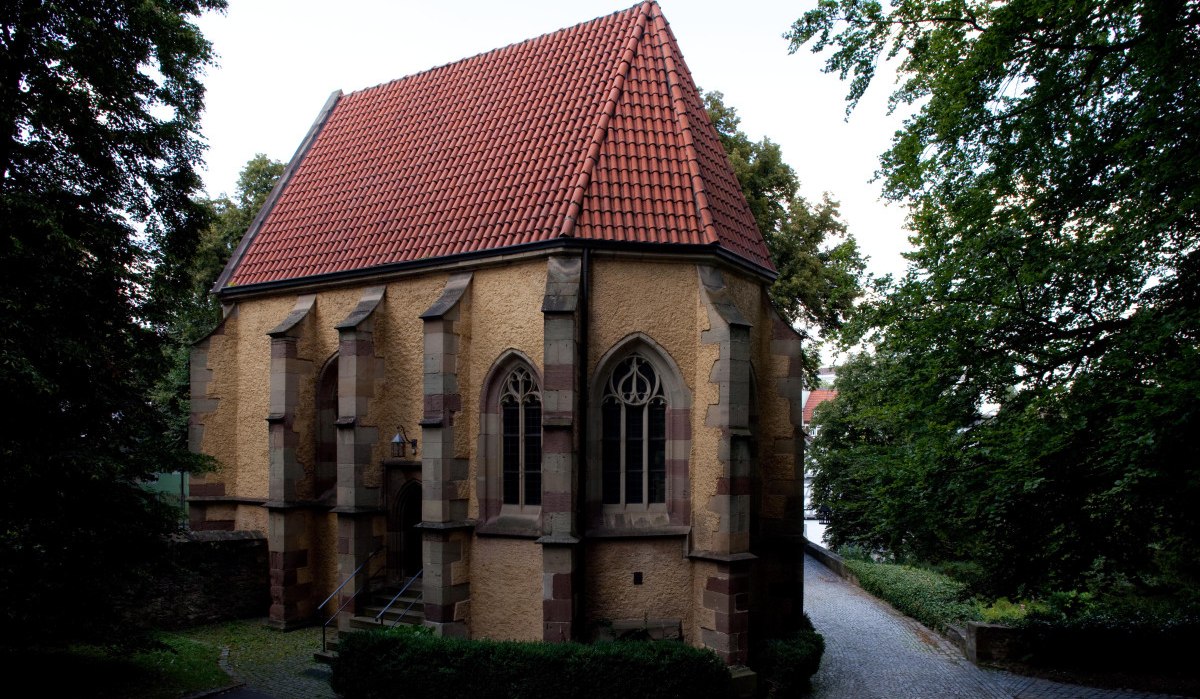 Kleine Kirche mit rotem Ziegeldach und gotischen Fenstern, umgeben von Bäumen und einem gepflasterten Weg., © Waiblingen - Stuttgart-Marketing GmbH Kleine Kirche mit rotem Ziegeldach und gotischen Fenstern, umgeben von Bäumen und einem gepflasterten Weg., © Waiblingen - Stuttgart-Marketing GmbH