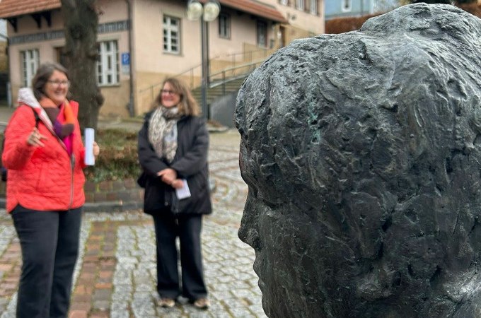 Zwei Frauen stehen neben einer Bronzebüste im Freien. Im Hintergrund ist ein Gebäude mit Fachwerk zu sehen., © PlochingenInfo Zwei Frauen stehen neben einer Bronzebüste im Freien. Im Hintergrund ist ein Gebäude mit Fachwerk zu sehen., © PlochingenInfo