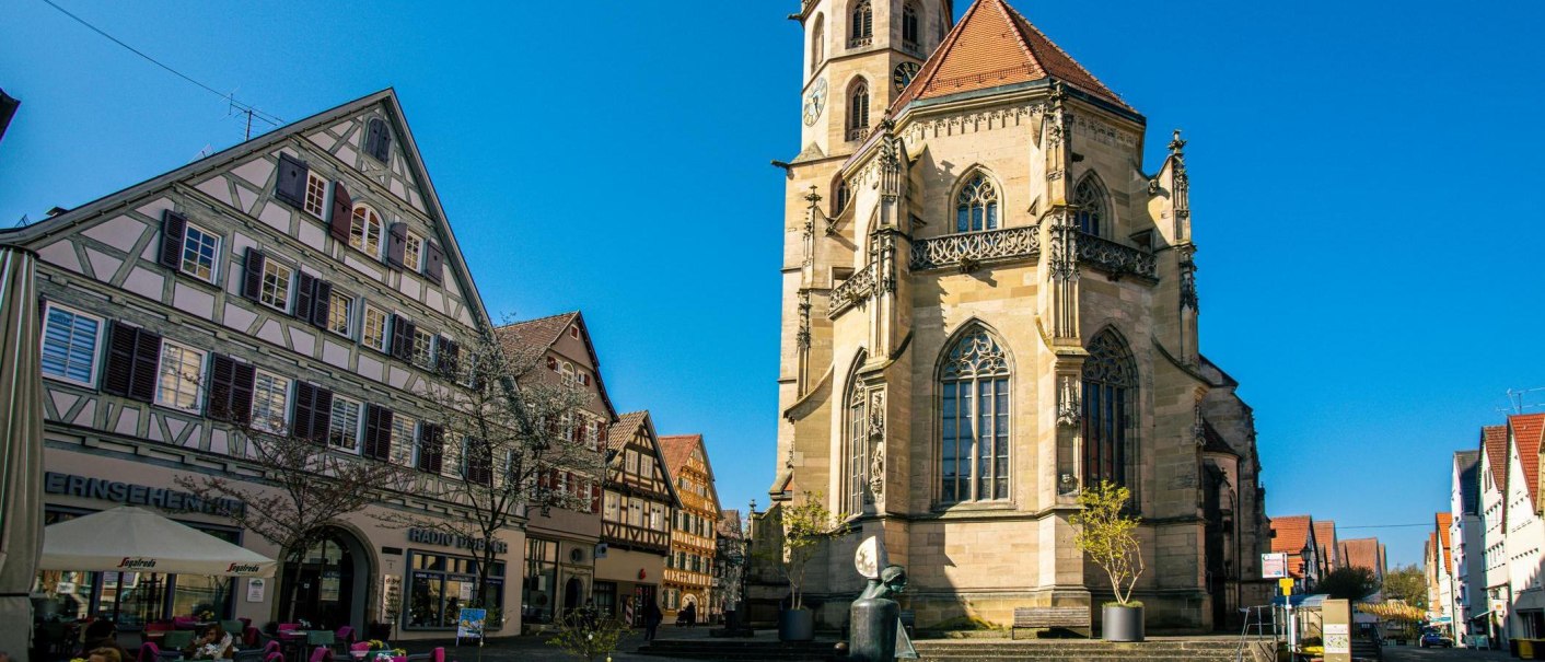 Die Stadtkirche in Schorndorf mit ihrem markanten Turm steht neben traditionellen Fachwerkh&auml;usern unter einem klaren blauen Himmel., &copy; Stuttgart-Marketing GmbH, Sarah Schmid