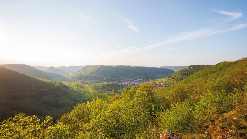 Panoramablick auf grüne Hügel und ein Tal mit einem Dorf. Die Sonne scheint von links, der Himmel ist klar mit wenigen Wolken., © SMG, Achim Mende Panoramablick auf grüne Hügel und ein Tal mit einem Dorf. Die Sonne scheint von links, der Himmel ist klar mit wenigen Wolken., © SMG, Achim Mende