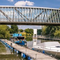 Moderne Glasbrücke über einem Fluss mit Booten und blühenden Pflanzen. Der Himmel ist klar und blau, was eine friedliche Sommeratmosphäre schafft., © Stuttgart-Marketing GmbH, Sarah Schmid