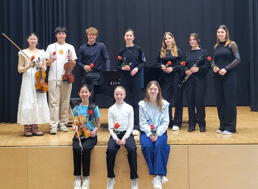 Junge Musikerinnen und Musiker posieren auf einer Bühne mit Instrumenten und Rosen. Sie tragen festliche Kleidung und lächeln in die Kamera., © Musikschule Pliezhausen