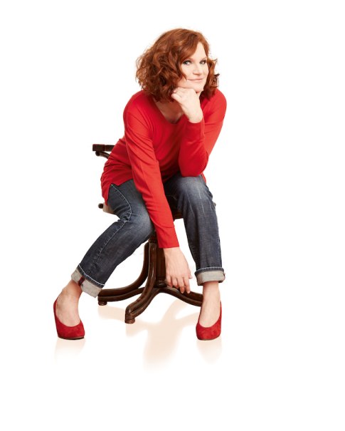 Frau mit roten Haaren, rotem Oberteil und Jeans sitzt lächelnd auf einem Stuhl. Sie trägt rote Schuhe und hat eine entspannte Haltung., © Stadtverwaltung Kirchheim unter Teck - Kulturring