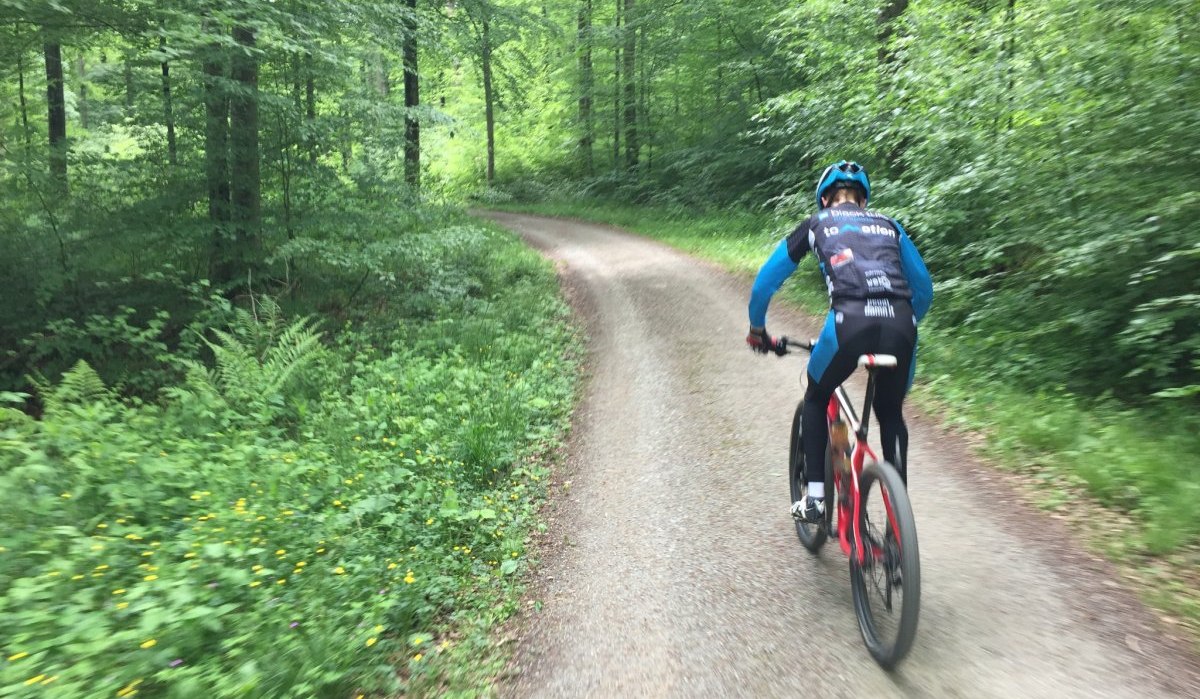Ein Radfahrer in blauer und schwarzer Sportkleidung f&auml;hrt auf einem schmalen Waldweg durch einen gr&uuml;nen, dichten Wald., &copy; Natur.Nah. Sch&ouml;nbuch & Heckeng&auml;u
