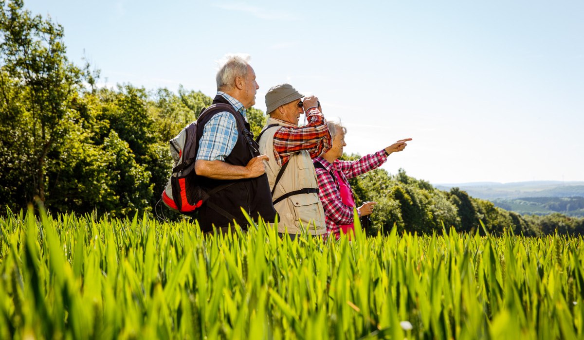 Drei ältere Personen wandern durch ein grünes Feld, zeigen in die Ferne und genießen die Natur. Sie tragen Freizeitkleidung und Rucksäcke., © Landkreis Göppingen Drei ältere Personen wandern durch ein grünes Feld, zeigen in die Ferne und genießen die Natur. Sie tragen Freizeitkleidung und Rucksäcke., © Landkreis Göppingen