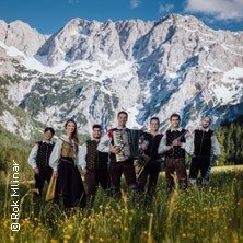 Musikgruppe in traditioneller Kleidung auf einer Wiese vor beeindruckender Bergkulisse., &copy; links im Bild