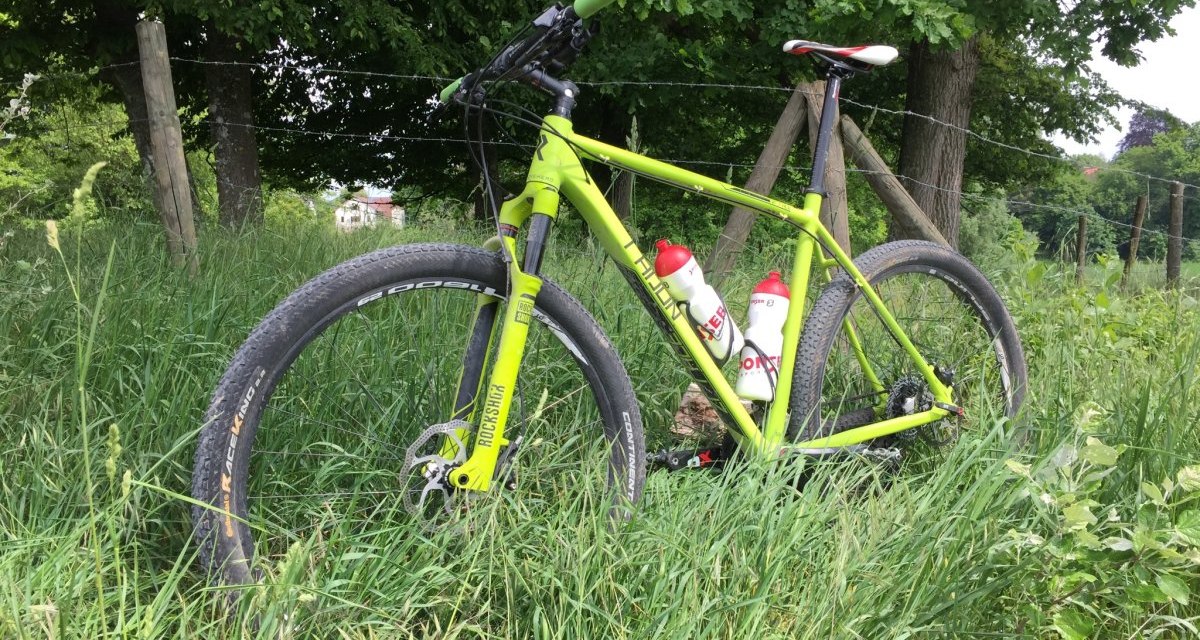 Ein gr&uuml;nes Mountainbike steht im hohen Gras neben einem Holzzaun, umgeben von B&auml;umen und Natur., &copy; www.pro-cycl.de