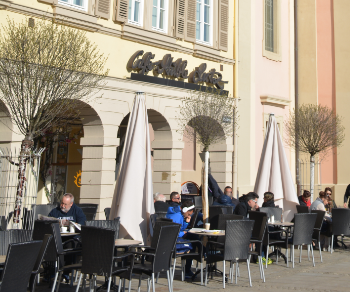 Gäste sitzen im Außenbereich des Café-Stüble Lutz, genießen das sonnige Wetter unter Sonnenschirmen vor einem historischen Gebäude., © Konditorei Lutz