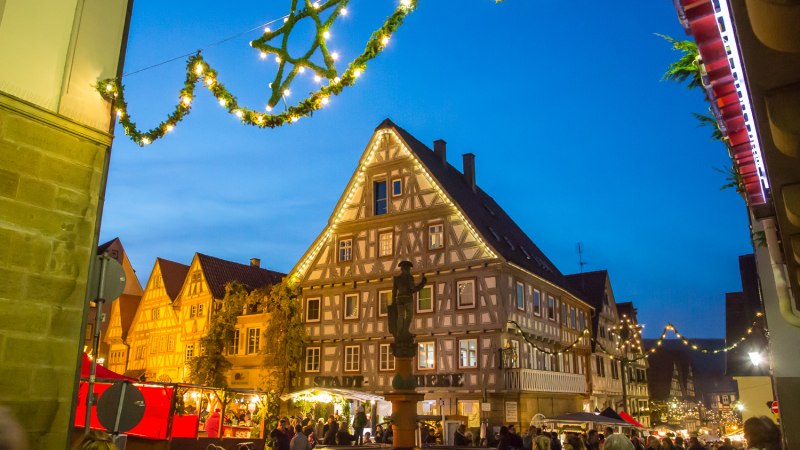 Weihnachtsmarkt in einer Altstadt mit beleuchteten Fachwerkhäusern und festlicher Dekoration. Menschen schlendern durch die Stände bei Abenddämmerung., © Stadt Besigheim Weihnachtsmarkt in einer Altstadt mit beleuchteten Fachwerkhäusern und festlicher Dekoration. Menschen schlendern durch die Stände bei Abenddämmerung., © Stadt Besigheim