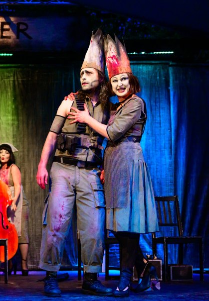 Zwei Schauspieler in auffälligen Kostümen und Gesichtsbemalung auf einer Bühne. Im Hintergrund spielt eine Musikerin Cello. Die Szene wirkt dramatisch., © René Löffler Zwei Schauspieler in auffälligen Kostümen und Gesichtsbemalung auf einer Bühne. Im Hintergrund spielt eine Musikerin Cello. Die Szene wirkt dramatisch., © René Löffler