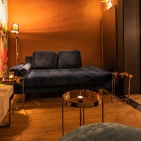 Gem&uuml;tliche Lounge mit blauer Couch, buntem Wandbild mit Affen und Pflanzen. Im Hintergrund eine Bar mit beleuchteten Regalen und Hockern., &copy; Holzmaler, Stuttgart