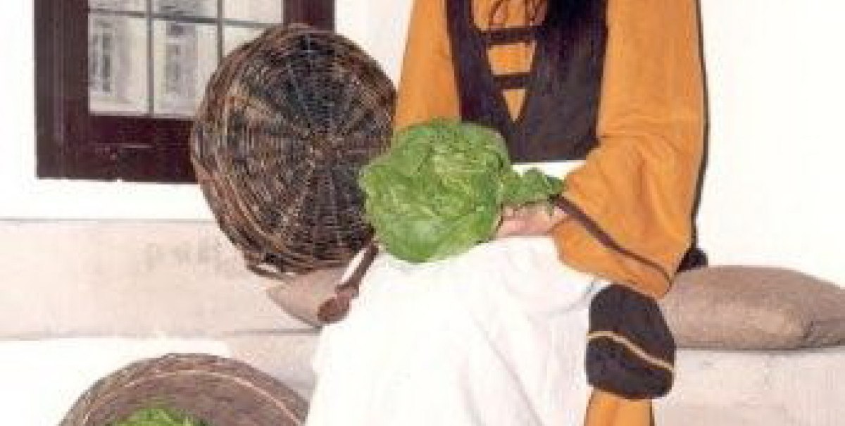 Eine Frau in historischer Kleidung sitzt mit einem Korb voller Gemüse im Residenzschloss Bad Urach.
