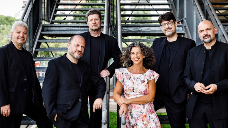 Sechs Personen in eleganter Kleidung posieren vor einer Metalltreppe im Freien. Eine Frau trägt ein geblümtes Kleid, die Männer tragen schwarze Anzüge., © Kultur- und Sportamt Stadt Bietigheim-Bissingen Sechs Personen in eleganter Kleidung posieren vor einer Metalltreppe im Freien. Eine Frau trägt ein geblümtes Kleid, die Männer tragen schwarze Anzüge., © Kultur- und Sportamt Stadt Bietigheim-Bissingen