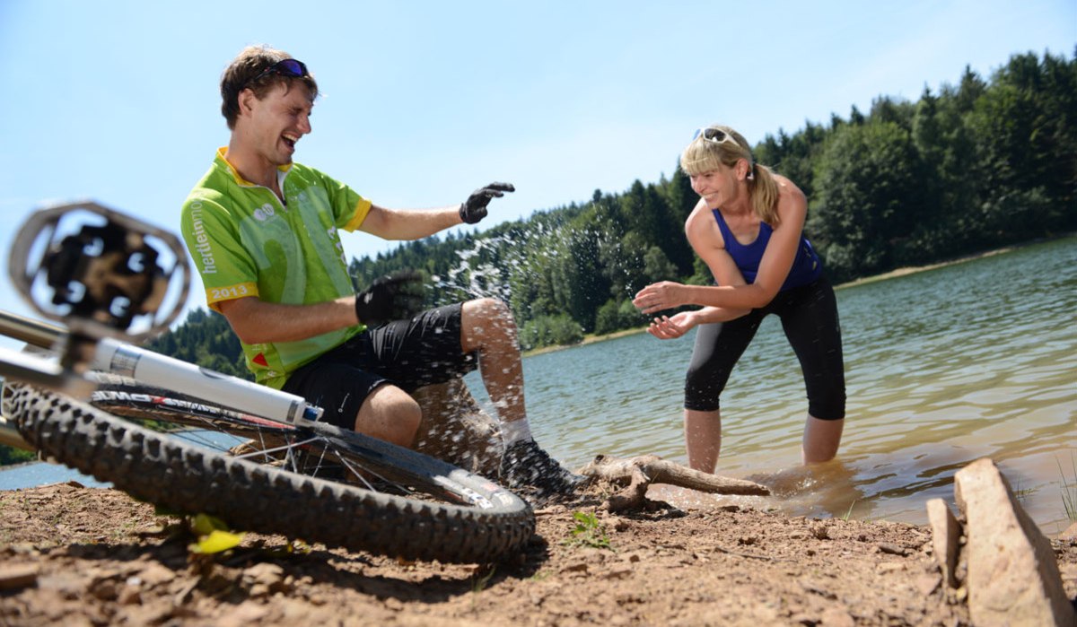 Zwei Personen am Ufer eines Sees, spielen lachend mit Wasser. Ein Fahrrad liegt im Vordergrund auf dem Boden., &copy; Landratsamt G&ouml;ppingen