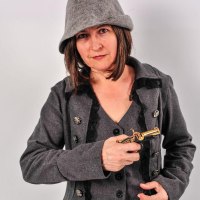 Eine Frau in einem grauen Mantel mit Kn&ouml;pfen und einem Filzhut h&auml;lt eine kleine Pistole in der Hand., &copy; Studio 1 Stuttgart