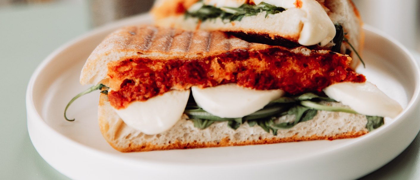 Ein Ciabatta-Sandwich mit Mozzarella und Rucola auf einem Teller, daneben eine Vase mit Trockenblumen., © L. Prestle/ Documenting Love Ein Ciabatta-Sandwich mit Mozzarella und Rucola auf einem Teller, daneben eine Vase mit Trockenblumen., © L. Prestle/ Documenting Love