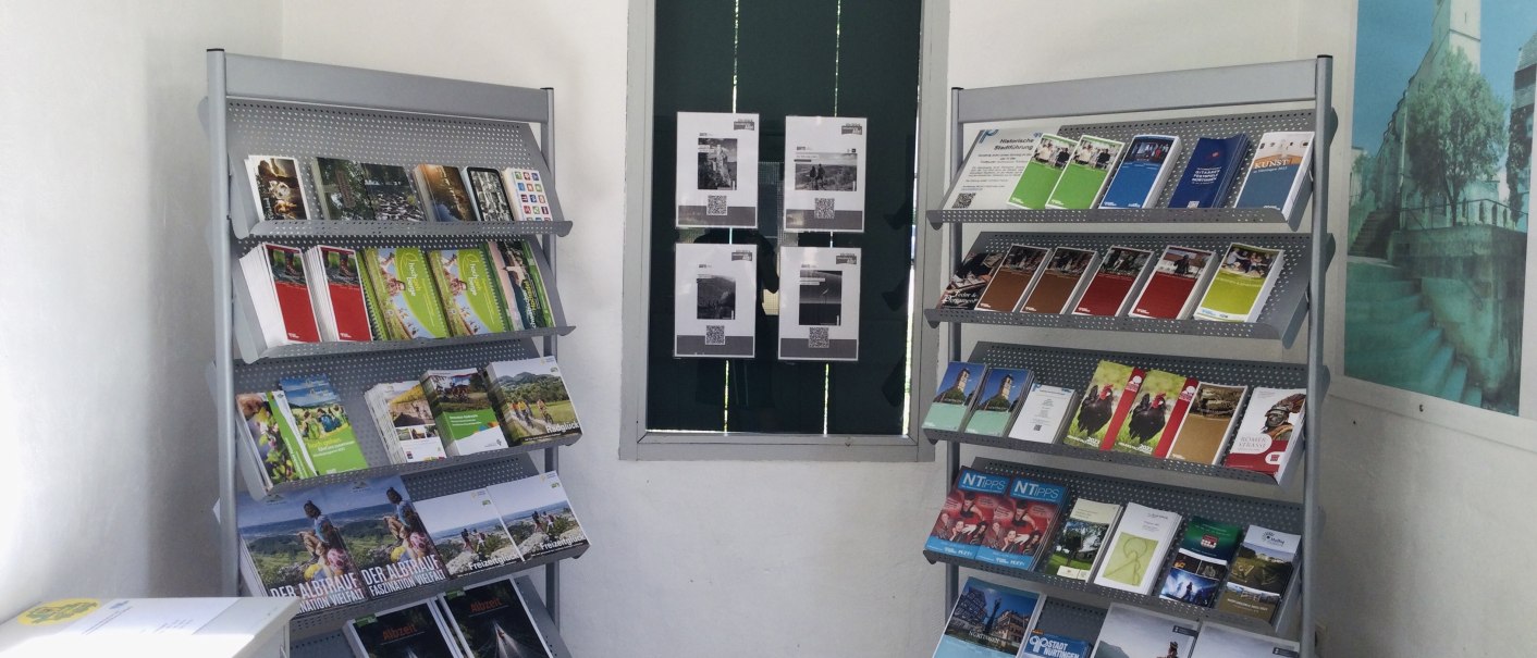 Innenansicht eines Informationspunkts mit zwei Broschürenregalen voller Flyer und Broschüren, einem Fenster und einem Wandbild., © J. Tubolzer