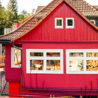 Ein rotes Gebäude mit weißen Fenstern, umgeben von grünen Bäumen. Ein Holzsteg führt am Gebäude vorbei., © Stuttgart-Marketing GmbH, Sarah Schmid