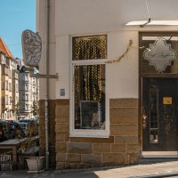Eingang des Café Seyffer’s an einer Straßenecke, dekoriert mit goldenen Girlanden und Pflanzen. Die Straße ist von Wohnhäusern gesäumt., © SMG, Sarah Schmid