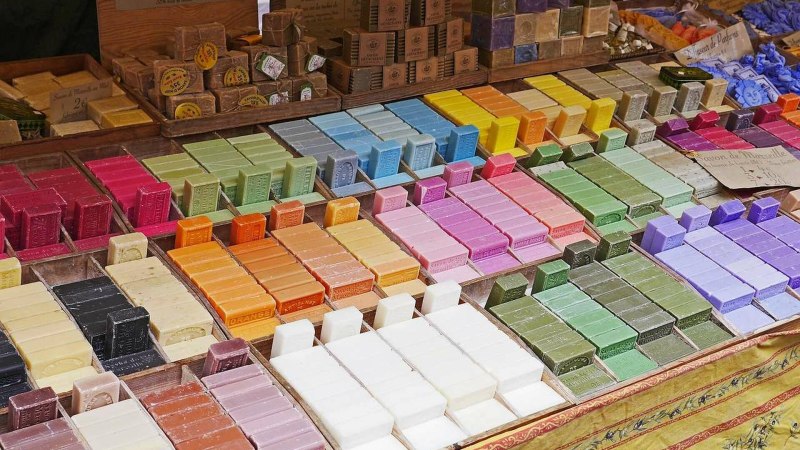 Bunte Seifenst&uuml;cke sind auf einem Marktstand in verschiedenen Farben und Formen ausgestellt. Der Stand ist reichhaltig best&uuml;ckt und wirkt einladend.