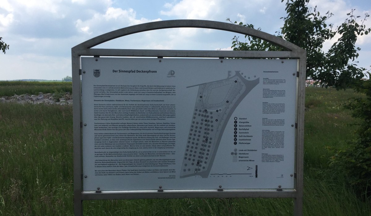 Infotafel zum Sinnespfad Deckenpfronn, umgeben von grüner Wiese und Bäumen unter einem bewölkten Himmel., © www.pro-cycl.de Infotafel zum Sinnespfad Deckenpfronn, umgeben von grüner Wiese und Bäumen unter einem bewölkten Himmel., © www.pro-cycl.de