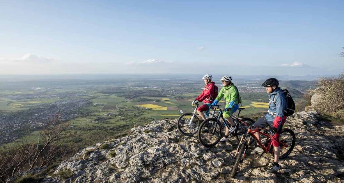 Drei Radfahrer stehen auf einem Felsen und blicken auf die weite Landschaft von Kirchheim unter Teck. Der Himmel ist klar und blau., © Schwäbische Alb Tourismusverband e.V. Drei Radfahrer stehen auf einem Felsen und blicken auf die weite Landschaft von Kirchheim unter Teck. Der Himmel ist klar und blau., © Schwäbische Alb Tourismusverband e.V.