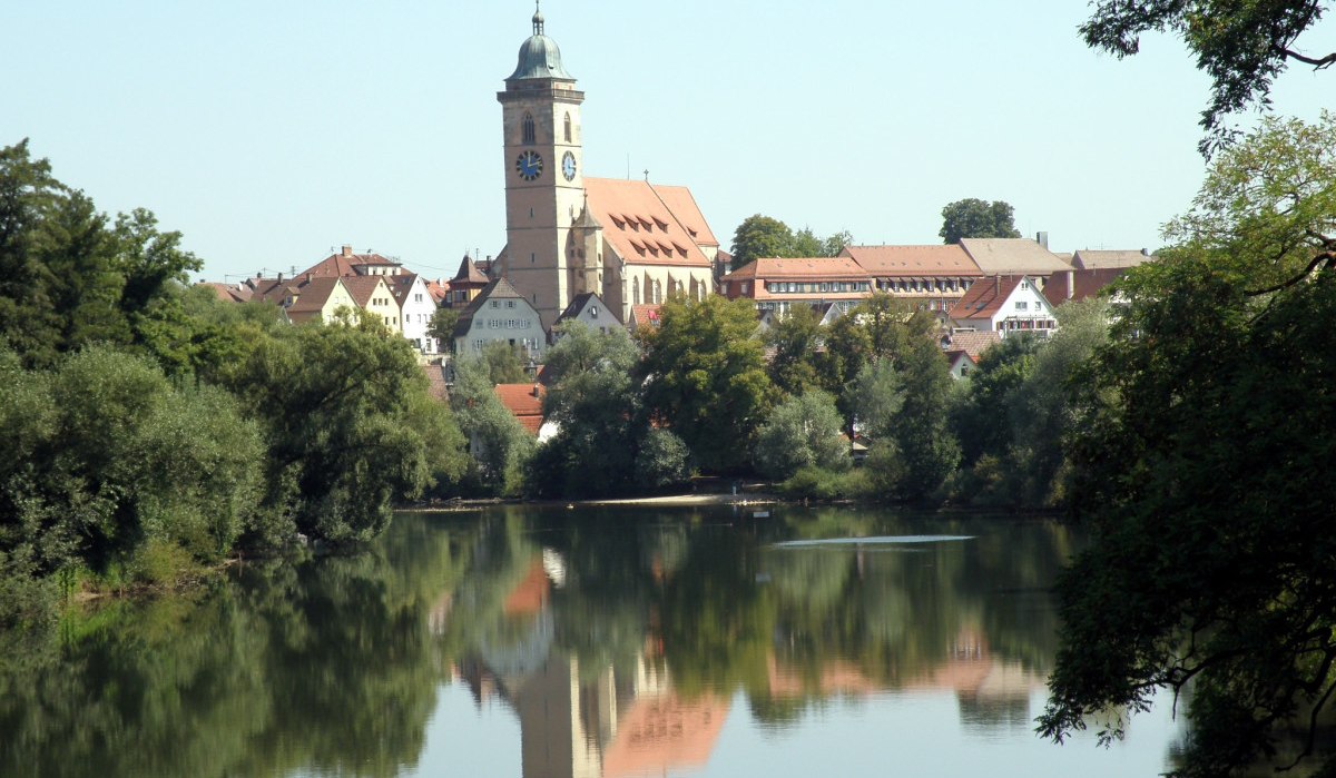 Nürtingen am Neckar mit einer Kirche im Zentrum, umgeben von Bäumen. Die Spiegelung der Stadt ist im ruhigen Wasser sichtbar., © Stadt Nürtingen