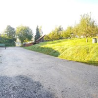 Ländliche Szene mit Holzstapeln an einem Gebäude, einem Anhänger und Obstbäumen auf einer Wiese bei sonnigem Wetter., © Mannschreck-Weine Ländliche Szene mit Holzstapeln an einem Gebäude, einem Anhänger und Obstbäumen auf einer Wiese bei sonnigem Wetter., © Mannschreck-Weine