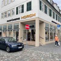 Parfümerie Godel in Nürtingen, Eckgebäude mit Schaufenstern, Autos parken davor, Passant geht vorbei., © Parfümerie Godel Parfümerie Godel in Nürtingen, Eckgebäude mit Schaufenstern, Autos parken davor, Passant geht vorbei., © Parfümerie Godel