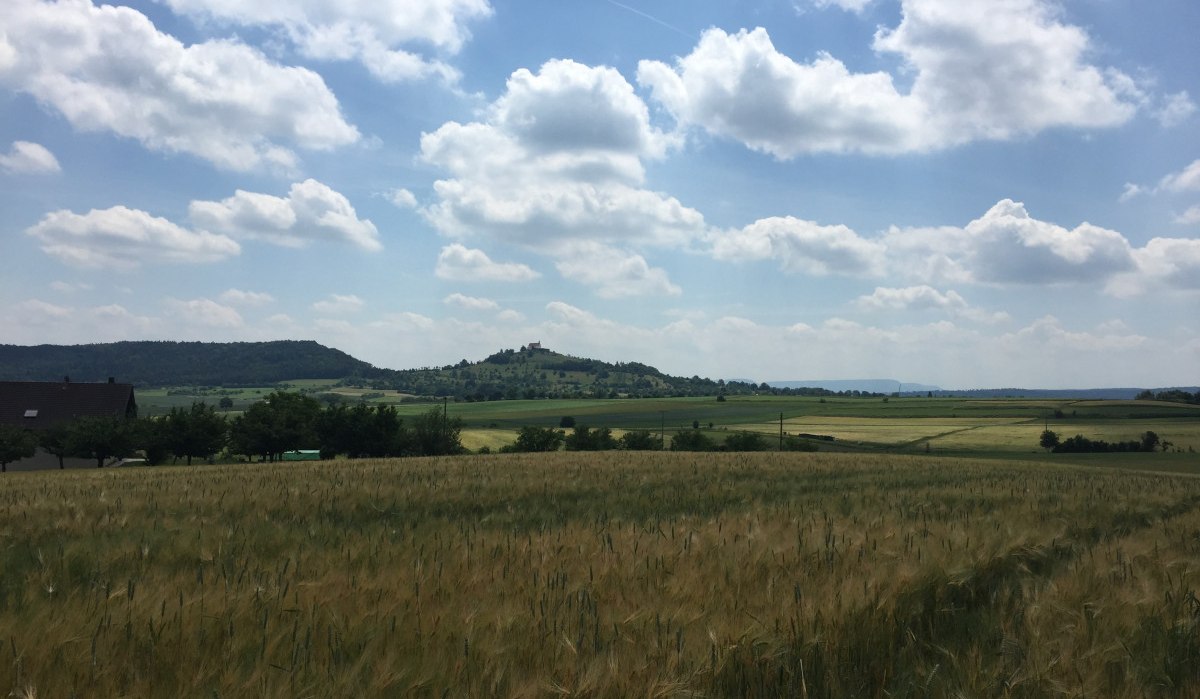 Weite Landschaft mit Feldern, im Hintergrund die Wurmlinger Kapelle auf einem Hügel unter blauem Himmel mit Wolken., © www.pro-cycl.de