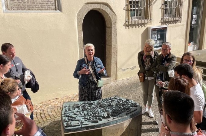 Eine Frau h&auml;lt eine F&uuml;hrung vor einem Stadtmodell im Freien, umgeben von einer Gruppe interessierter Zuh&ouml;rer., &copy; Eigenbetrieb Tourismus und Citymanagement Schorndorf