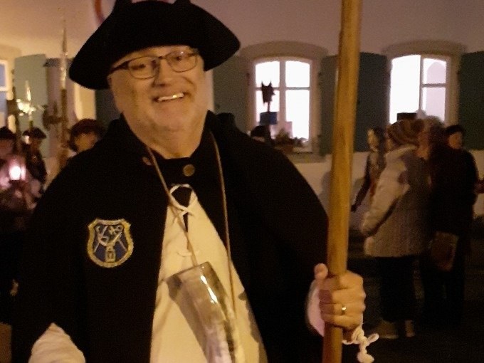 Ein Mann in Nachtwächterkleidung mit Hut und Stab lächelt in die Kamera. Im Hintergrund sind Menschen und ein beleuchtetes Gebäude zu sehen., © WTM GmbH Waiblingen Ein Mann in Nachtwächterkleidung mit Hut und Stab lächelt in die Kamera. Im Hintergrund sind Menschen und ein beleuchtetes Gebäude zu sehen., © WTM GmbH Waiblingen