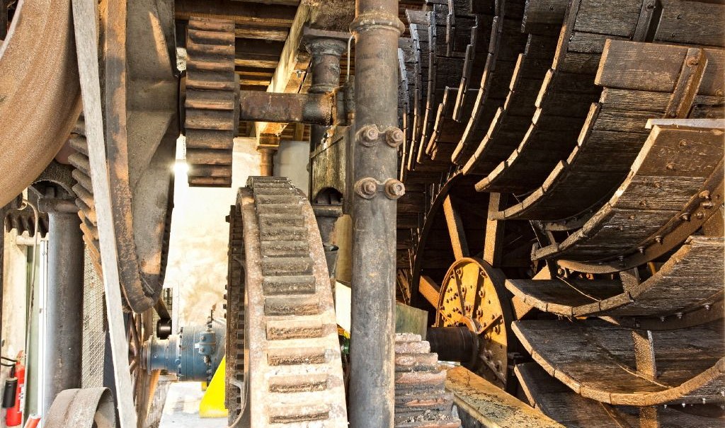 Nahaufnahme eines alten Wasserrads mit gro&szlig;en Zahnr&auml;dern und Holzelementen in einem industriellen Umfeld., &copy; ECOINN Hotel am Campus
