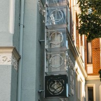 Fassade eines Geb&auml;udes mit verzierten Elementen und einem Schild mit Logo. Ein Baum wirft Schatten auf die Wand. Klare, sonnige Atmosph&auml;re., &copy; SMG, Sarah Schmid