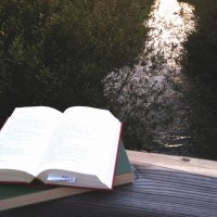 Ein aufgeschlagenes Buch liegt auf einem Holzbalken, w&auml;hrend die Abendsonne den Fluss im Hintergrund beleuchtet., &copy; &copy; Brigitte H&auml;usler