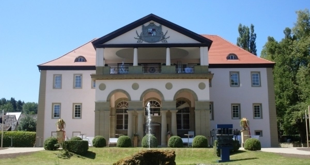 Schloss D&auml;tzingen mit symmetrischer Fassade, rotem Dach und S&auml;ulen. Im Vordergrund ein gepflegter Garten mit Springbrunnen., &copy; Gemeinde Grafenau