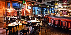 Gemütliche Brauerei mit Kupferkesseln, Holztischen und -stühlen. Barbereich mit roten Hockern, warmes Ambiente durch Beleuchtung und Dekor., © Parkhotel Stuttgart Messe-Airport