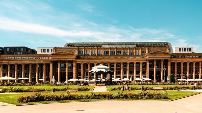 Der Königsbau in Stuttgart mit klassizistischer Fassade und Glasdach, umgeben von Grünflächen und Spaziergängern bei sonnigem Wetter., © Stuttgart-Marketing GmbH, Sarah Schmid Der Königsbau in Stuttgart mit klassizistischer Fassade und Glasdach, umgeben von Grünflächen und Spaziergängern bei sonnigem Wetter., © Stuttgart-Marketing GmbH, Sarah Schmid