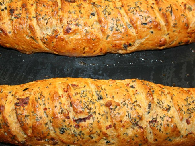 Zwei goldbraune Baguettes mit Kräutern und Gewürzen, frisch gebacken auf einem schwarzen Backblech., © Kultweine-Kochwelten-Kunstücke - Kochschule Sonja Lenz Zwei goldbraune Baguettes mit Kräutern und Gewürzen, frisch gebacken auf einem schwarzen Backblech., © Kultweine-Kochwelten-Kunstücke - Kochschule Sonja Lenz