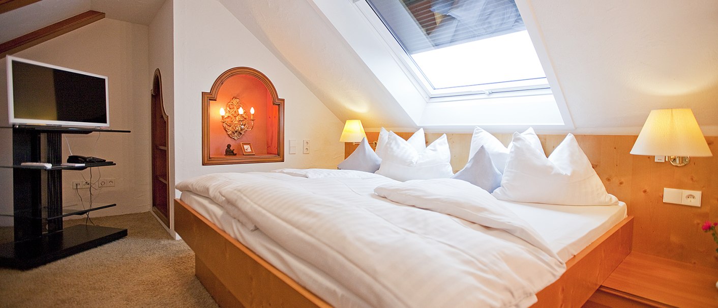 Gemütliches Schlafzimmer mit Dachfenster, Doppelbett, Fernseher und warmem Licht. Holzmöbel und Teppichboden schaffen eine einladende Atmosphäre., © Hotel Krone Gemütliches Schlafzimmer mit Dachfenster, Doppelbett, Fernseher und warmem Licht. Holzmöbel und Teppichboden schaffen eine einladende Atmosphäre., © Hotel Krone